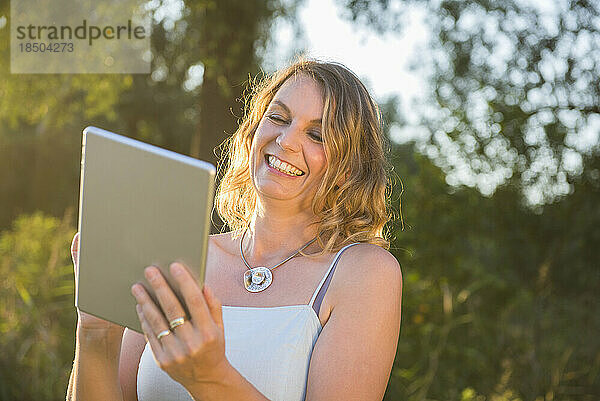 Fröhliche Frau lächelt  während sie draußen in der Natur ein digitales Tablet benutzt  Bayern  Deutschland