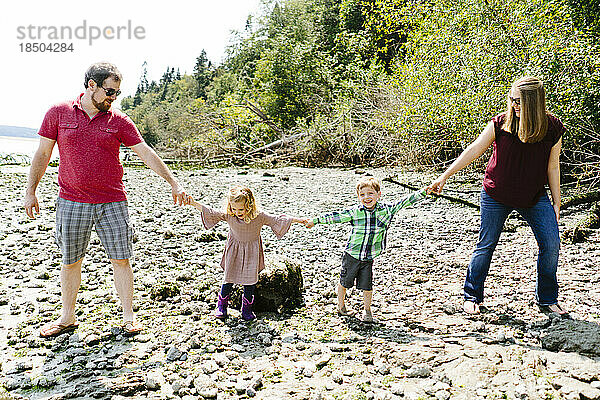 Geradeaus Porträt einer vierköpfigen Familie  die sich an einem felsigen Strand an den Händen hält