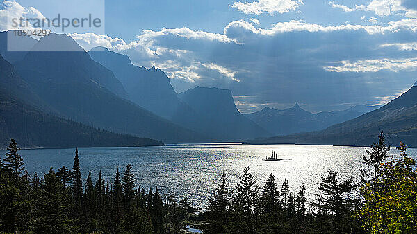 Die Sonne durchdringt stürmische Wolken über dem See im Glacier National Park