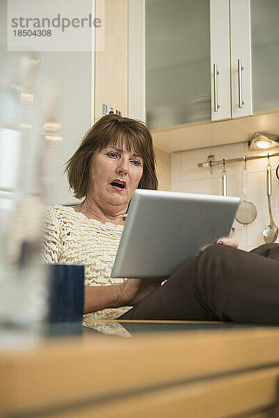 Ältere Frau sieht schockiert aus  während sie ein digitales Tablet in der Küche benutzt  München  Bayern  Deutschland