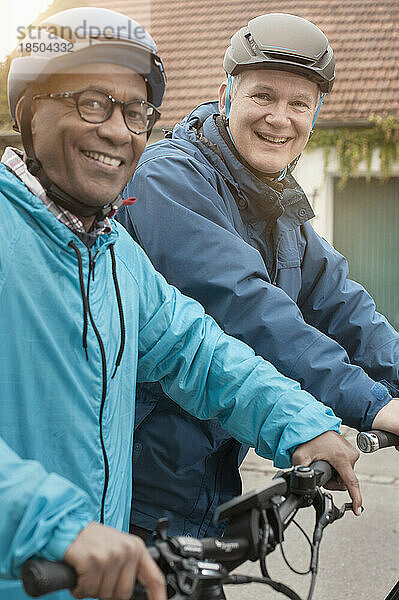 Male friends cycling and smiling on street  Bavaria  Germany