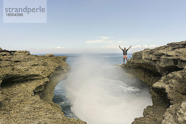 Junger Mann steht auf einer Felsformation vor den Meereswellen  Nusa Lembongang  Bali  Indonesien