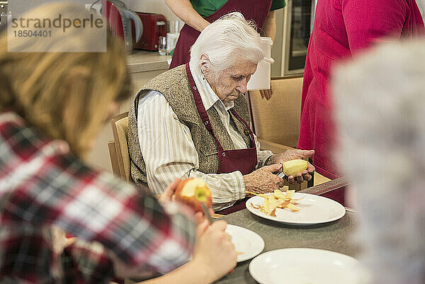 Ältere Frauen mit Mädchen schälen Apfel im Pflegeheim