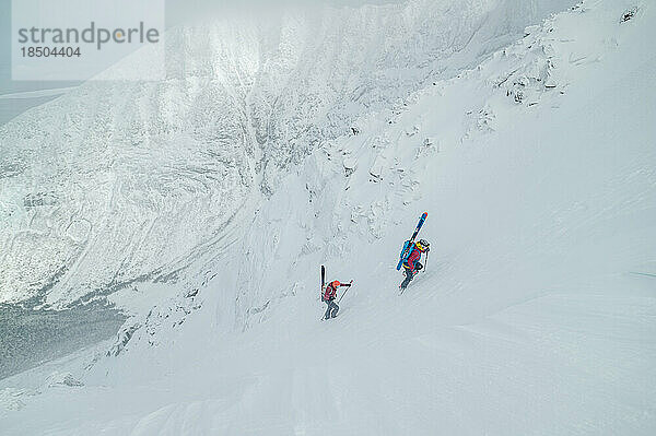 Backcountry-Skifahrer erklimmen eine steile Schlucht mit großen Bergen dahinter