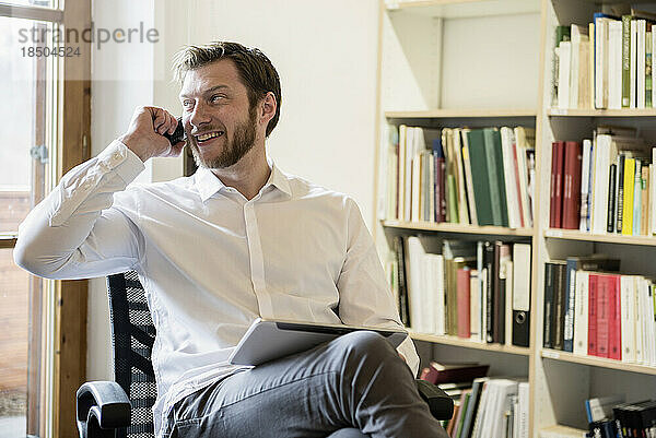 Mittlerer erwachsener Geschäftsmann nutzt digitales Tablet und telefoniert in einem Büro  Bayern  Deutschland