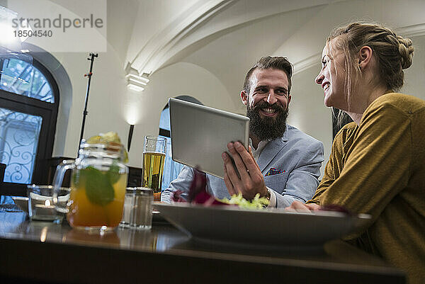 Lächelndes Paar nutzt digitales Tablet im Restaurant