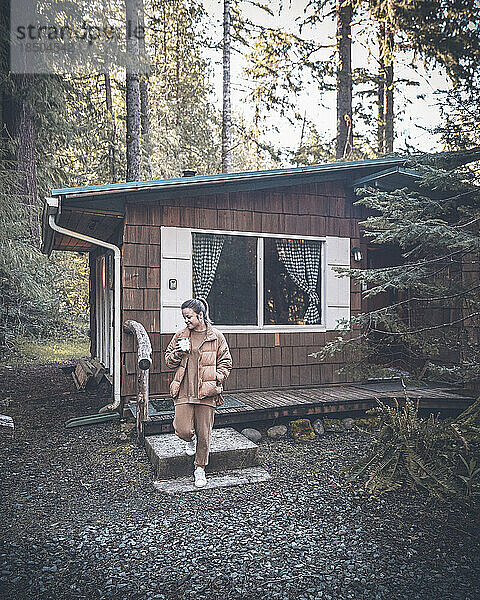 Eine Frau steht mit einer Tasse Kaffee in einer Waldhütte