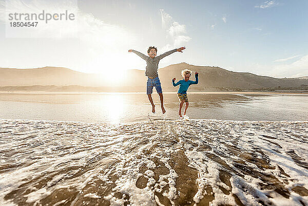 Zwei glückliche Jungen springen am Strand ins Wasser