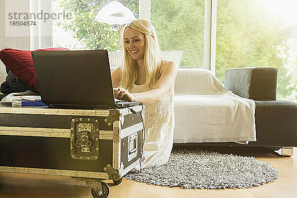 Schöne junge Frau benutzt Laptop im Wohnzimmer und lächelt  München  Bayern  Deutschland