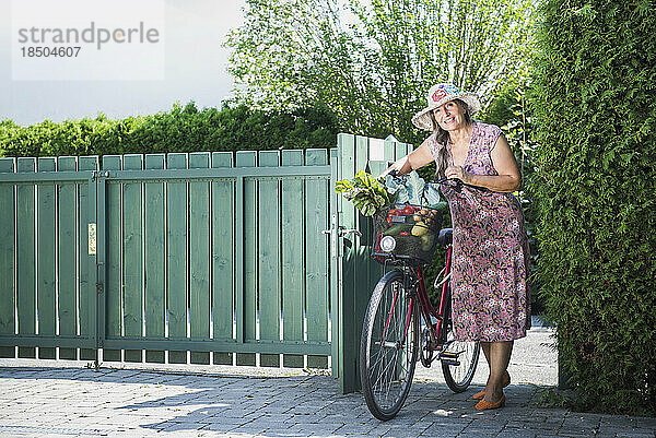 Ältere Frau betritt Gartentor mit Fahrrad und Gemüse  Bayern  Deutschland