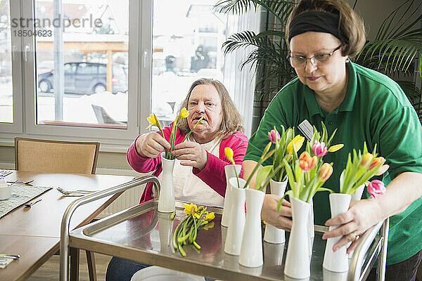 Hausmeister und ältere Frau arrangieren Blumen und Vasen im Pflegeheim
