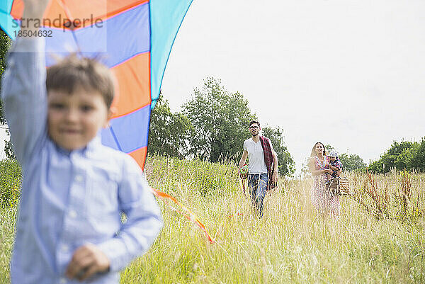 Familie spaziert mit Picknickkorb und Drachen auf der Wiese auf dem Land  Bayern  Deutschland
