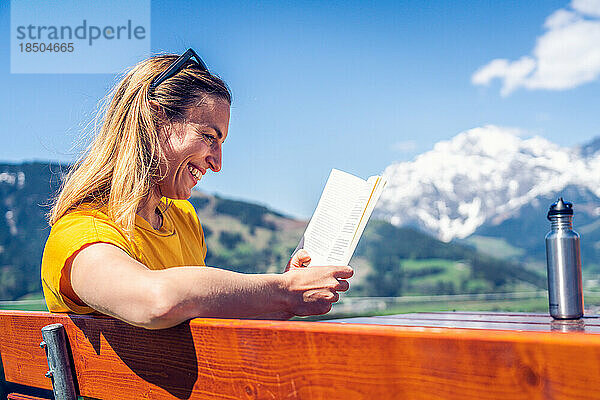 Junges schönes und glückliches Mädchen  das auf einer Bank ein Buch liest  Mounta