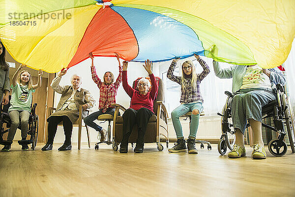 Mädchen und ältere Frauen machen im Seniorenheim sanfte Sportübungen mit Fallschirm