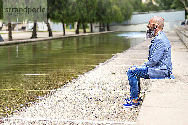 Ein bärtiger Mann mittleren Alters mit zunehmender Glatze sitzt in einem Park und entspannt sich