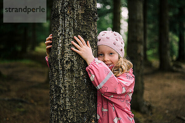 Kleines blondes Kind im Wald umarmt Baum