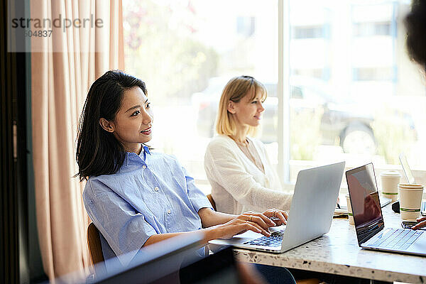 Lächelnde Geschäftsfrau mit Laptop  die neben einem Kollegen im Café sitzt