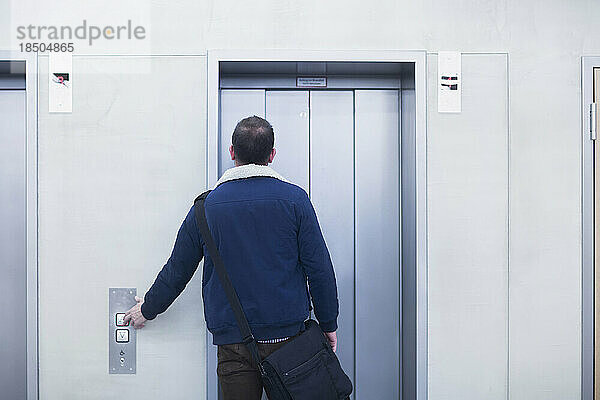 Rückansicht eines Geschäftsmannes  der den Aufzugsknopf in einem Büro drückt  Freiburg im Breisgau  Baden-Württemberg  Deutschland