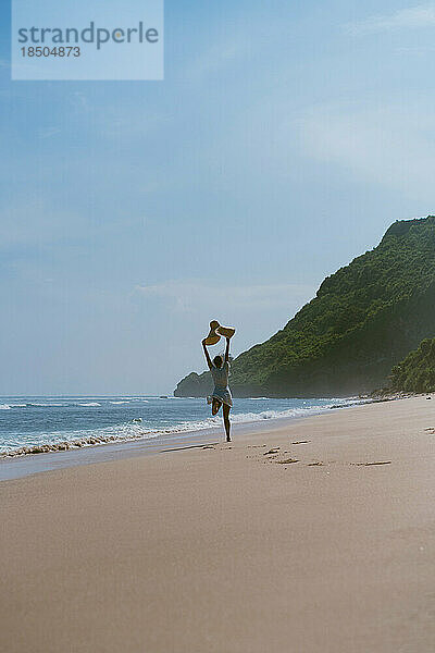 Junge glückliche freie Frau mit Strohhut tanzt auf dem Meer.