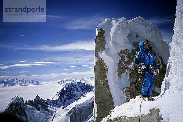 Ein Bergsteiger hält auf einem Felsvorsprung am Nordgrat des Cerro Torre inne  mit Torre Egger im Hintergrund  im argentinischen Patagonien.