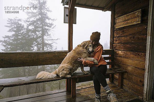 Niedlicher  flauschiger Hund und Mädchen umarmen sich auf der Veranda der Hütte