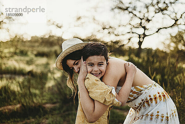 Seitenansicht einer jungen Mutter und ihres kleinen Sohnes  die sich auf dem Feld umarmen und lächeln
