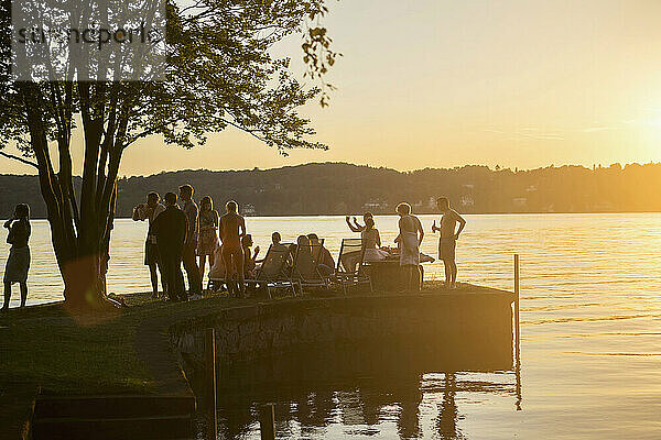 Gruppe junger Freunde feiert bei Sonnenuntergang am Seeufer  Bayern  Deutschland