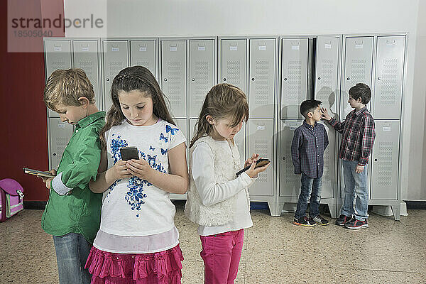 Schulkinder nutzen Smartphone im Flur in der Nähe von Schließfächern  Bayern  Deutschland