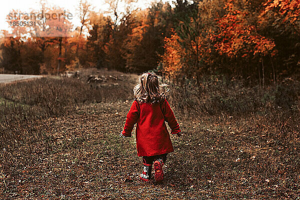 Kind geht an einem schönen Herbsttag im roten Mantel draußen spazieren