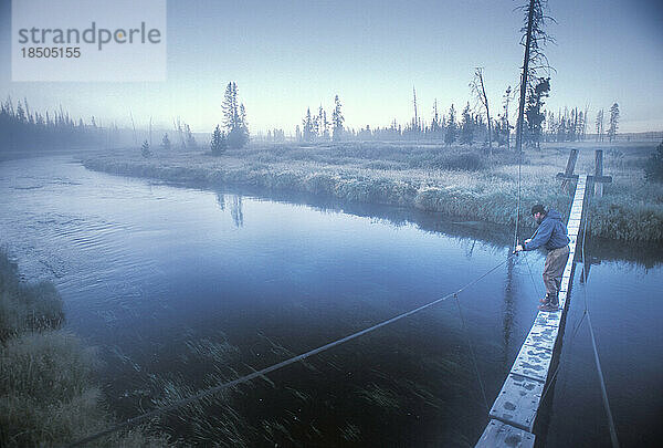Ein Fliegenfischer sucht von einer alten Holzbrücke aus nach Forellen.
