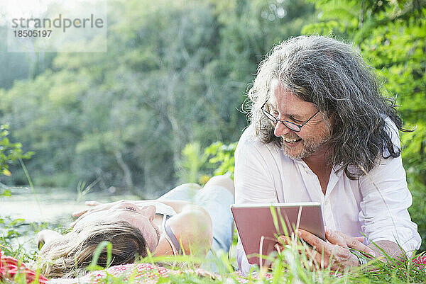 Paar liegt nebeneinander mit digitalem Tablet am See  Deutschland