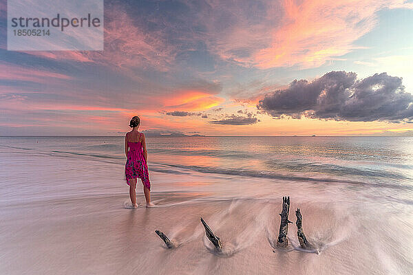 Frau am tropischen Strand blickt bei Sonnenuntergang auf das Karibische Meer