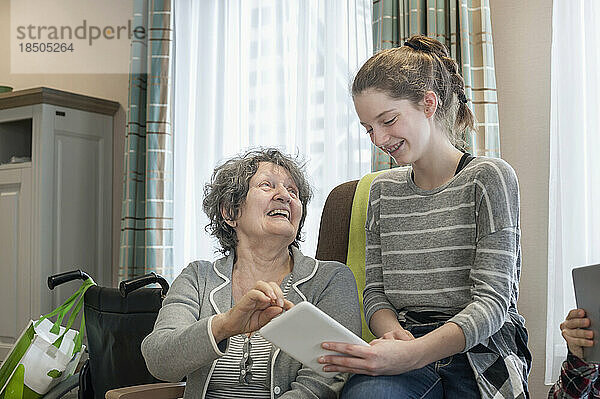Ältere Frauen mit Enkelin nutzen digitales Tablet im Pflegeheim