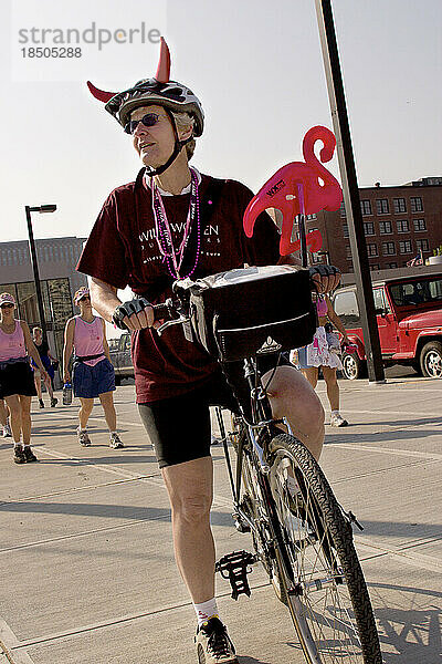 Woman on a bicycle with funny props helps work crew at a breast cancer walk.