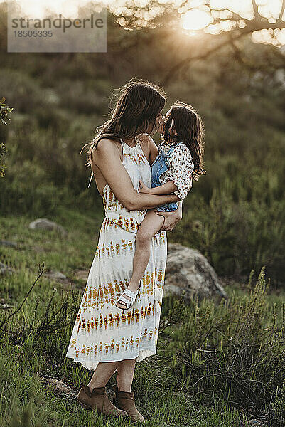 Ganzkörperansicht von Mutter und Tochter  die sich auf einem sonnigen Feld küssen