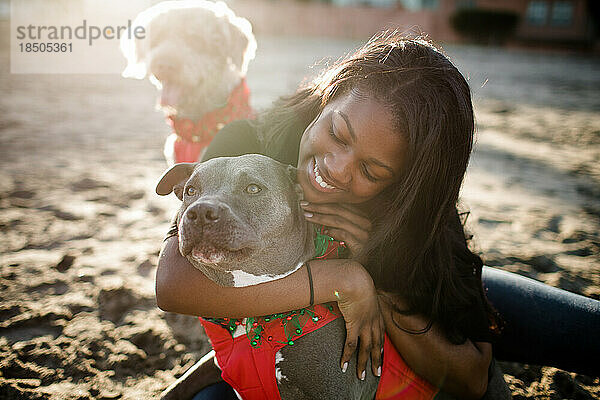 Young girl hugging pitbull on beach at sunset