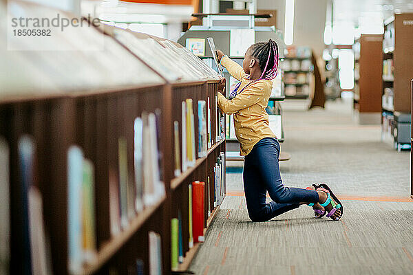 Junges afroamerikanisches Mädchen sucht im Bücherregal nach einem Buch