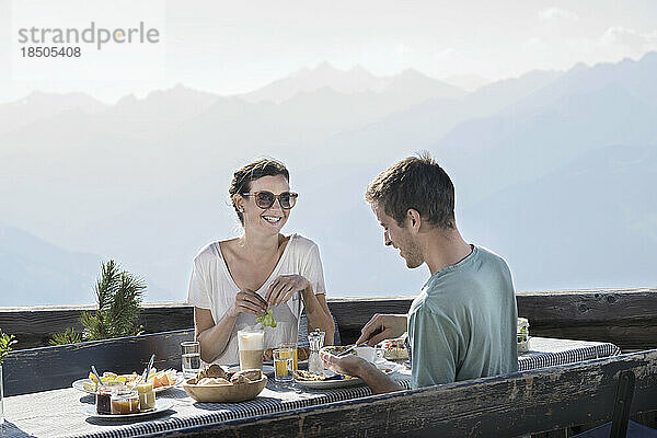 Junges Paar beim Frühstück auf der Terrasse und lächelnd  Zillertal  Tirol  Österreich