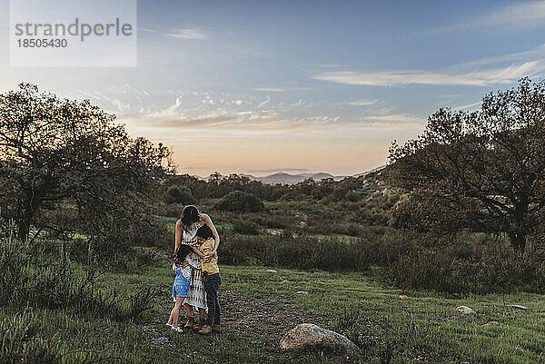 Landschaft mit jungen Müttern und Kindern  die sich unter blauem Himmel auf dem Feld umarmen