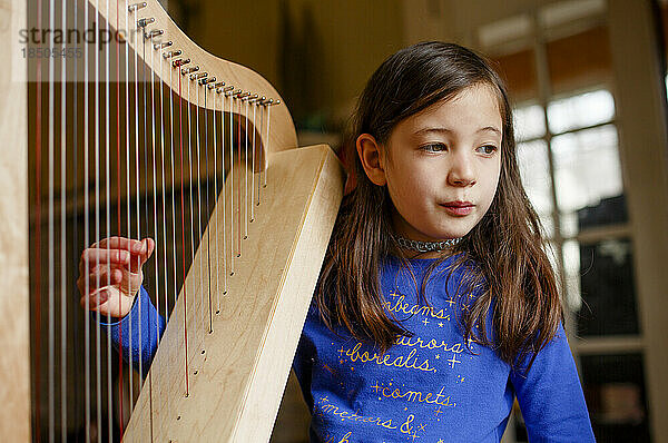 Ein junges Mädchen zupft drinnen an den Saiten einer kleinen Harfe