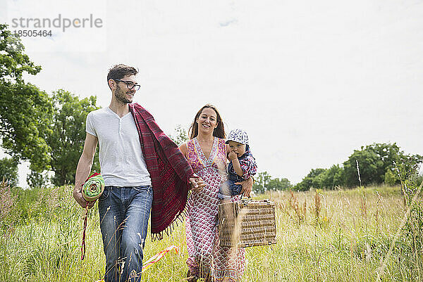Familie mit Picknickkorb spaziert auf der Wiese und lächelt  Bayern  Deutschland