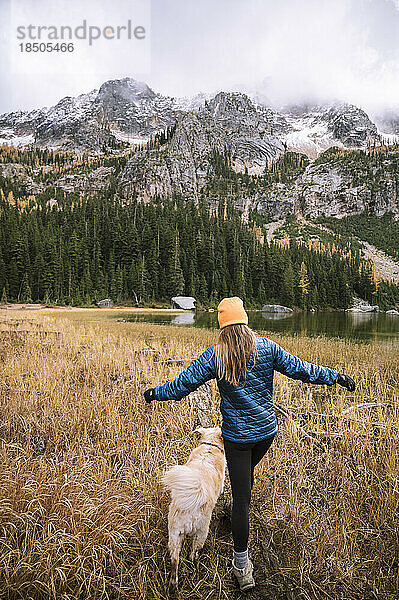 Wanderin und ihr Hund neben einem Alpensee mit Lärchen