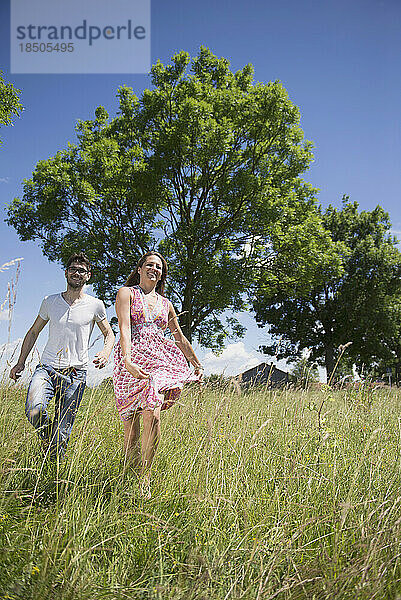 Mitte erwachsenes Paar läuft durch Gras auf einer Wiese auf dem Land  Bayern  Deutschland