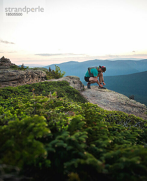 Trailrunner-Mann bindet Schuhe mit Bergen hinter sich bei Sonnenaufgang