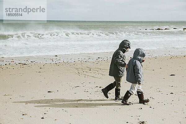 Zwei Jungen gehen mit tosenden Wellen am Strand entlang