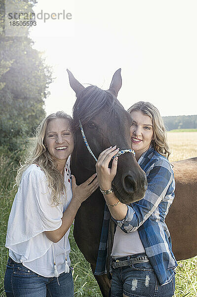 Porträt zweier Frauen  die ein Pferd auf der Wiese streicheln und lächeln  Bayern  Deutschland