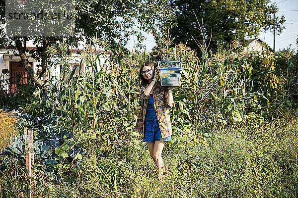 Das Bauernmädchen hält einen Korb voller Gemüse auf dem grünen Bauernhof