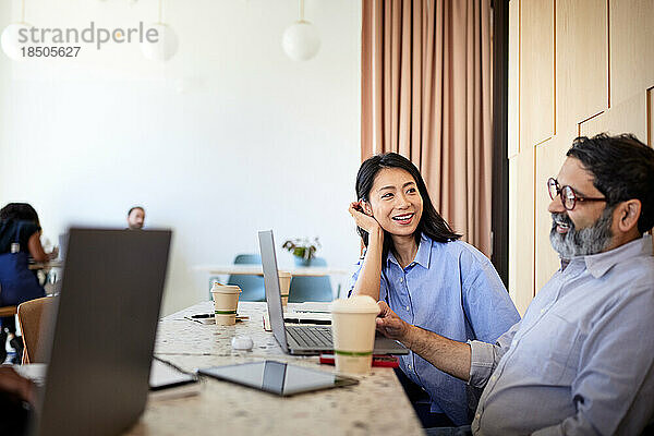 Geschäftsfrau spricht mit männlichem Kollegen mit Laptop im Café