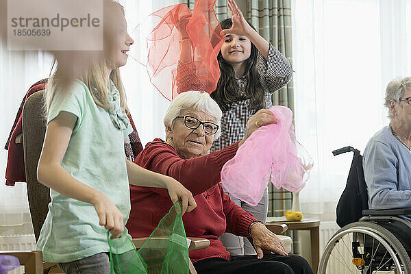 Mädchen und ältere Frau machen im Pflegeheim sanfte Sportübungen mit Stoff