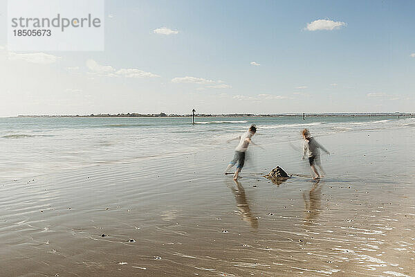 Zwei Kinder laufen am Strand vor blauem Himmel